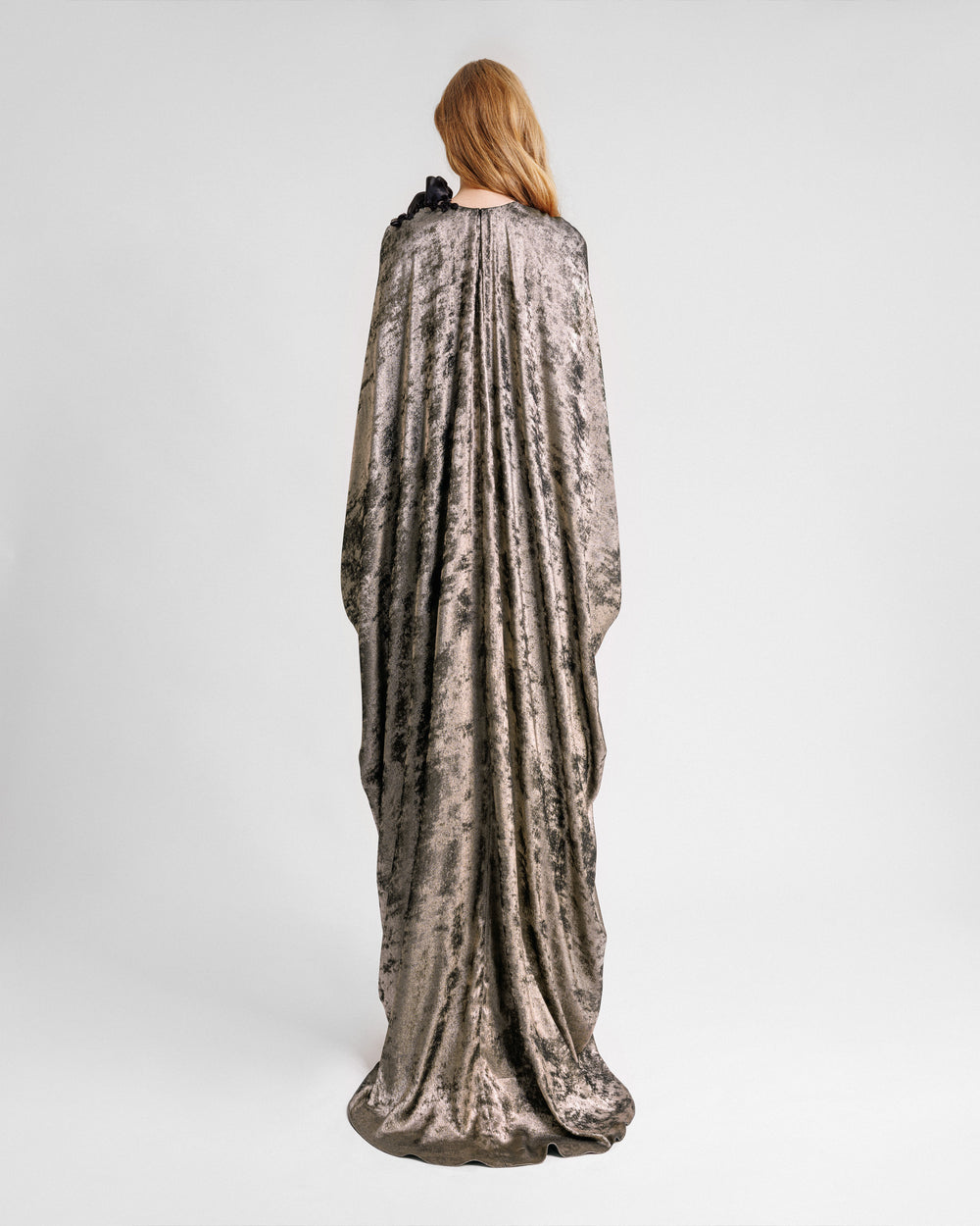 The back of a loose-cut kaftan dress with floral draping on the shoulder.