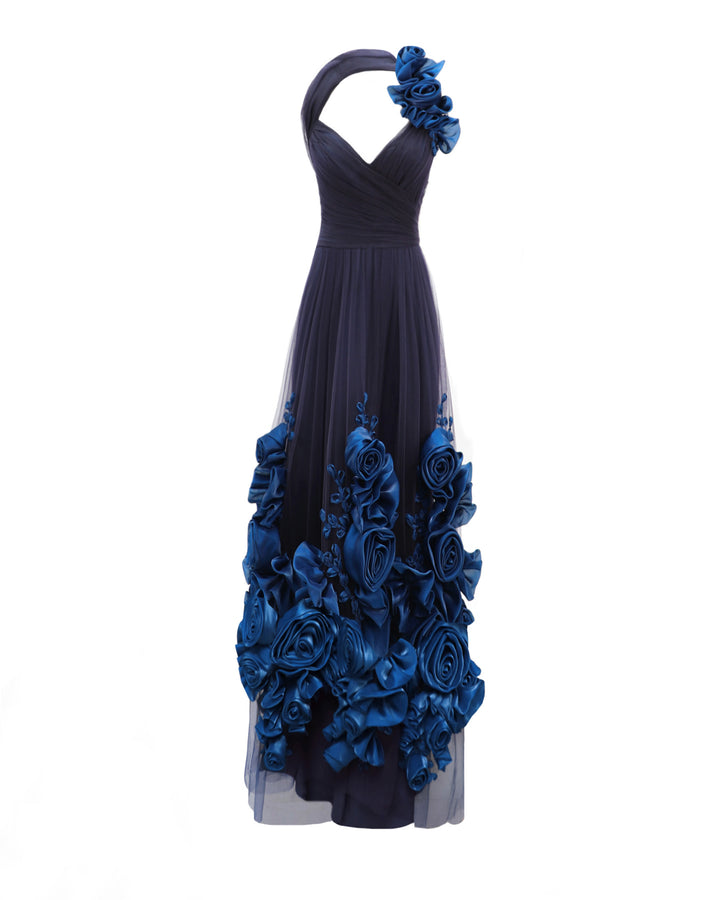 An asymmetrical neckline flared evening dress in navy draped tulle with floral draping on the shoulder and hemline.