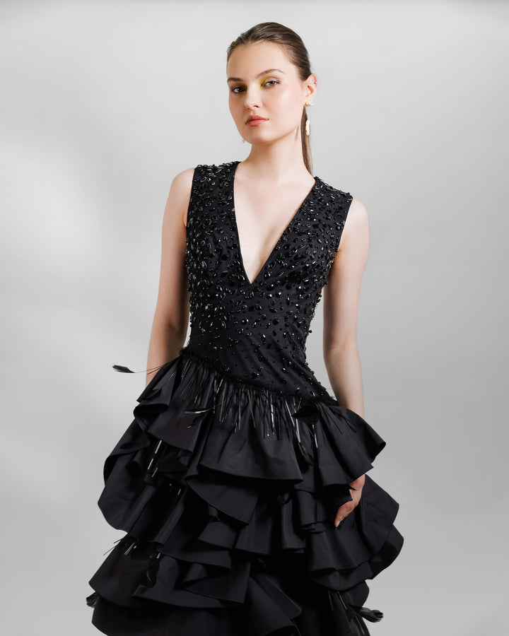 A close-up of a V-neckline black evening dress with beadings and ruffled taffeta layers.