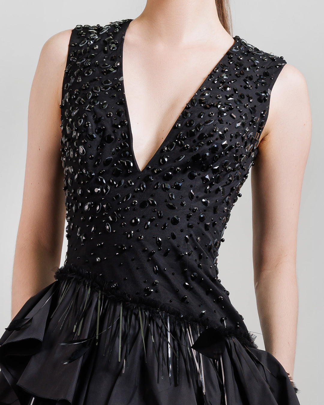 A close-up of a V-neckline black evening dress with beadings and ruffled taffeta layers.