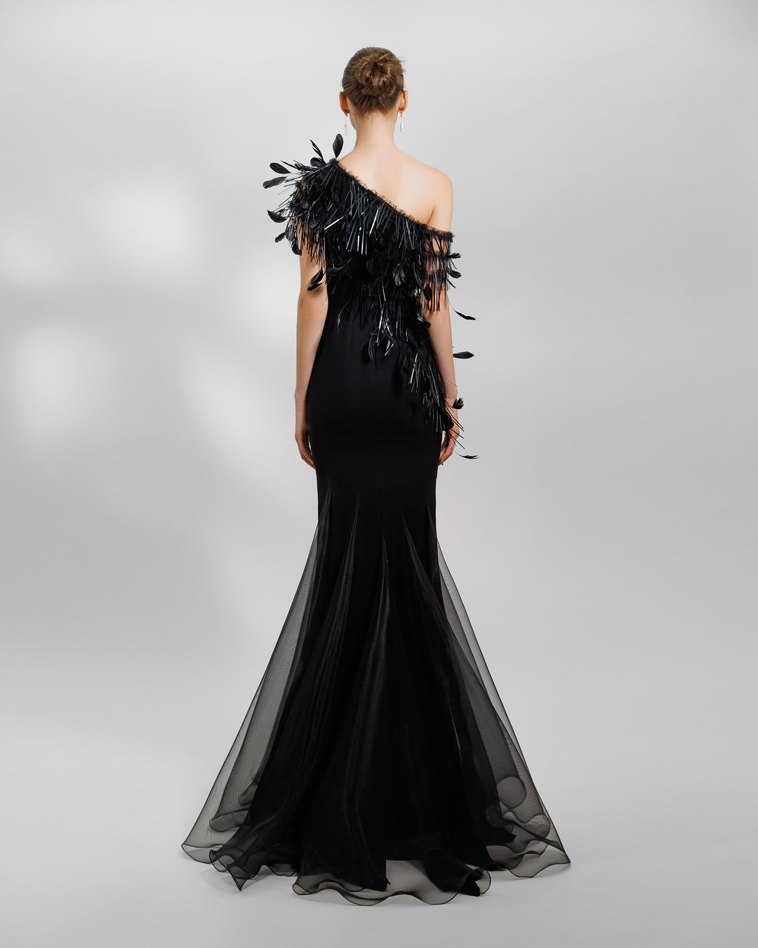 The back of an asymmetrical feather neckline black evening dress with flared organza stripes.