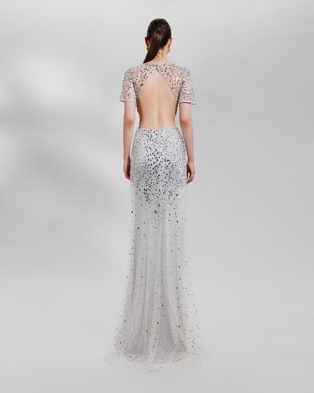 The back of a fully beaded tulle long evening dress, featuring a straight slim cut. Under the tulle a sweetheart shaped bodice with side cut outs, short sheer sleeves and an open back, all in grey color.