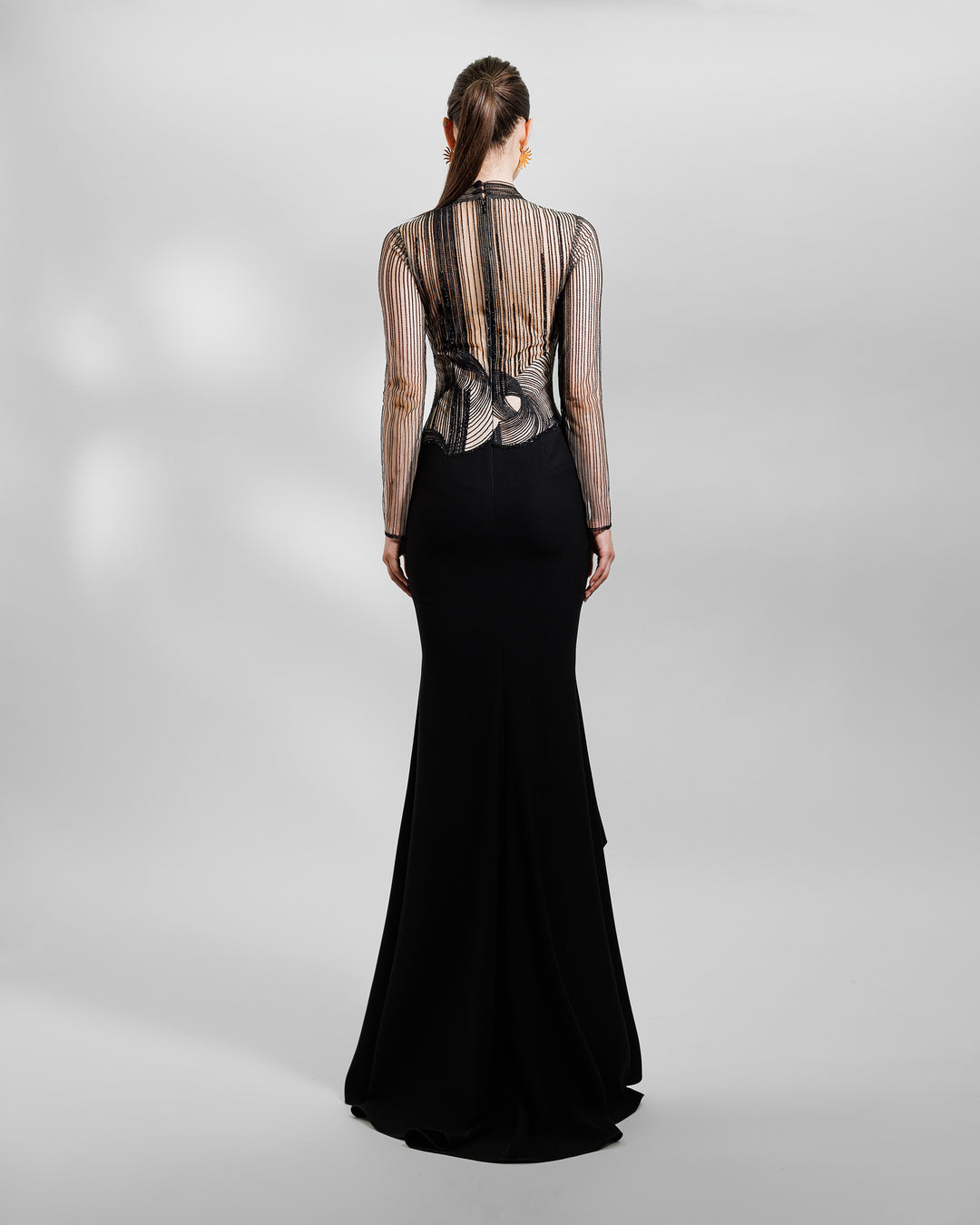 The back of a long-sleeve slim-cut black evening dress featuring an embroidered upper part lace slits on the sides.