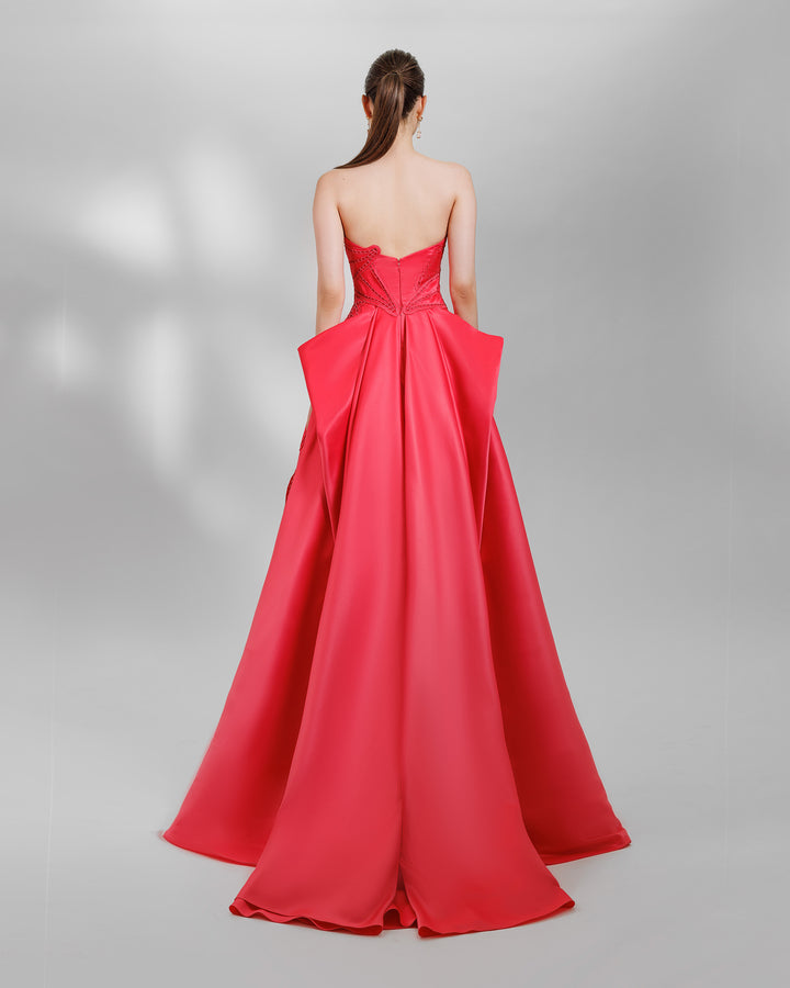 The back of a strapless red evening dress with laser-cut details, a wide flared cut, and draping at the back.