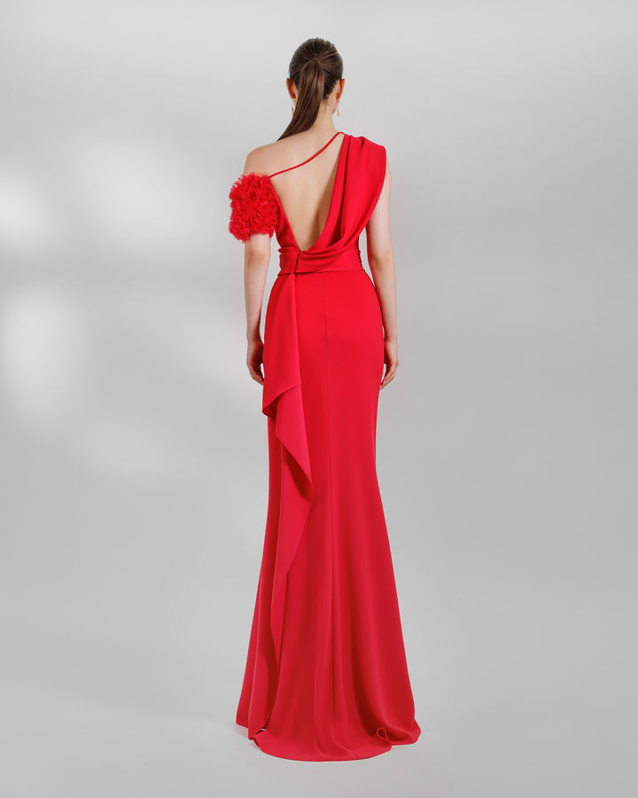 The back of a one-shoulder red evening dress with a rushed organza short sleeve, draped open back, and a ruffled slit.