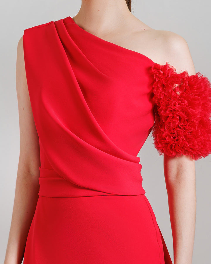 A close-up of a a one-shoulder red evening dress with a rushed organza short sleeve, draped open back, and a ruffled slit.