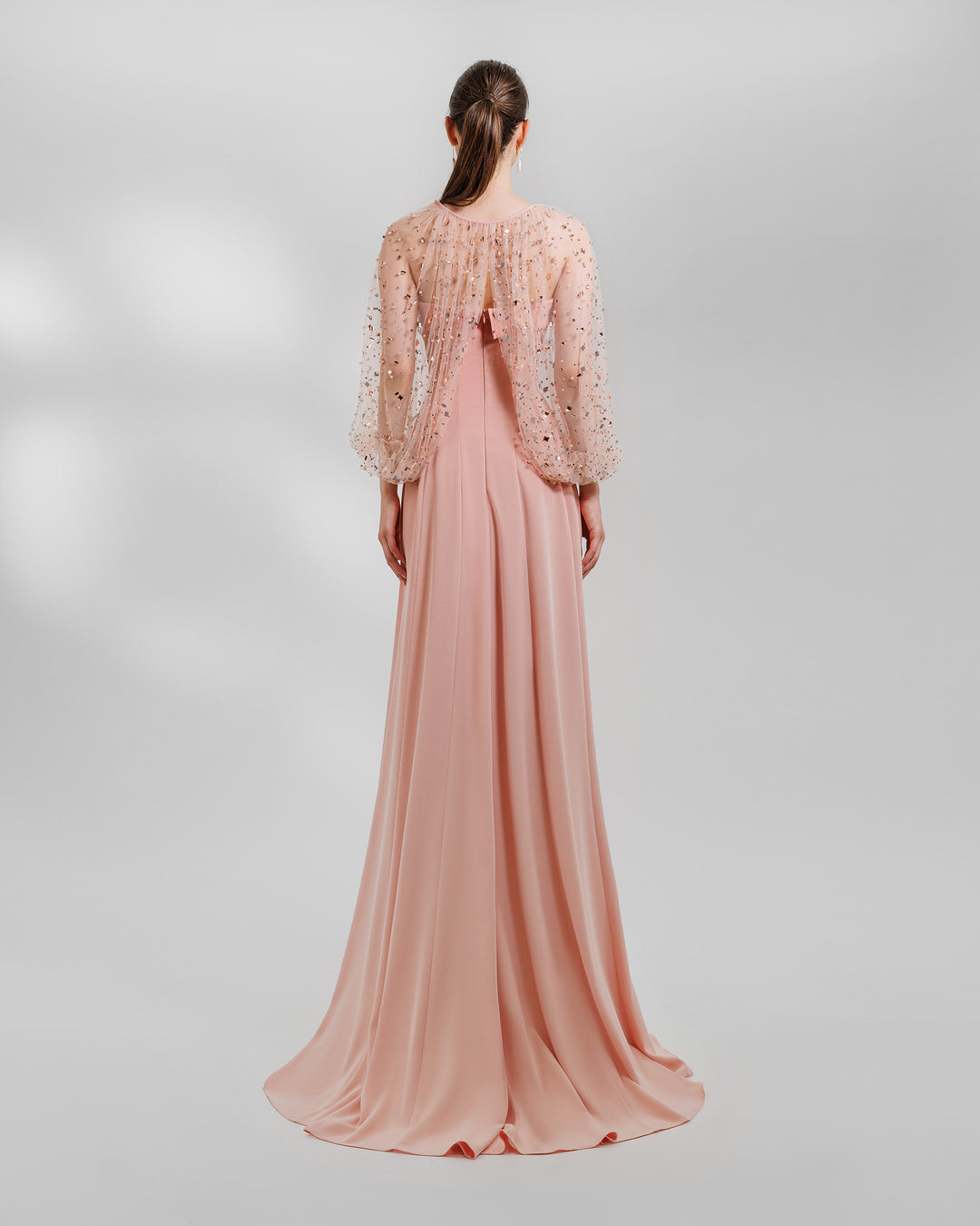 The back of a strapless flared long peach crepe evening dress, featuring a folded strap. Over it a fully beaded tulle Bolero.