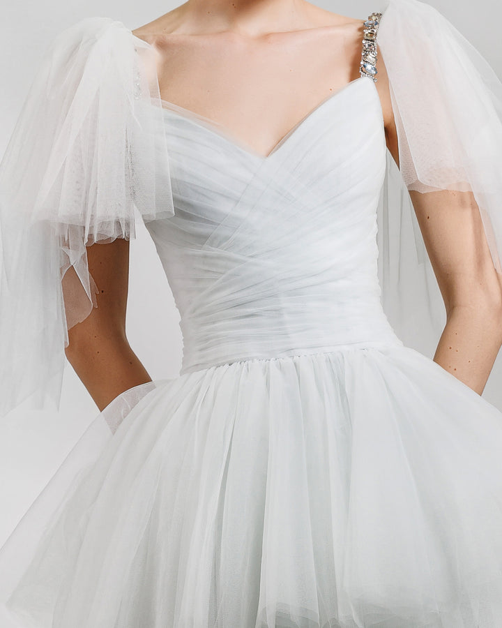 A close-up of a fully ruffled grey tulle evening dress featuring a draped corset accentuating the waist and a sweetheart neckline. It also features beaded straps and ruffled tulle on the shoulders.