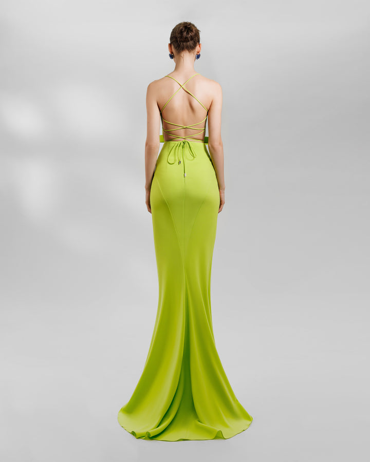 The back of an open-laced back long lime evening dress featuring a statement bow on the waist and a middle slit.