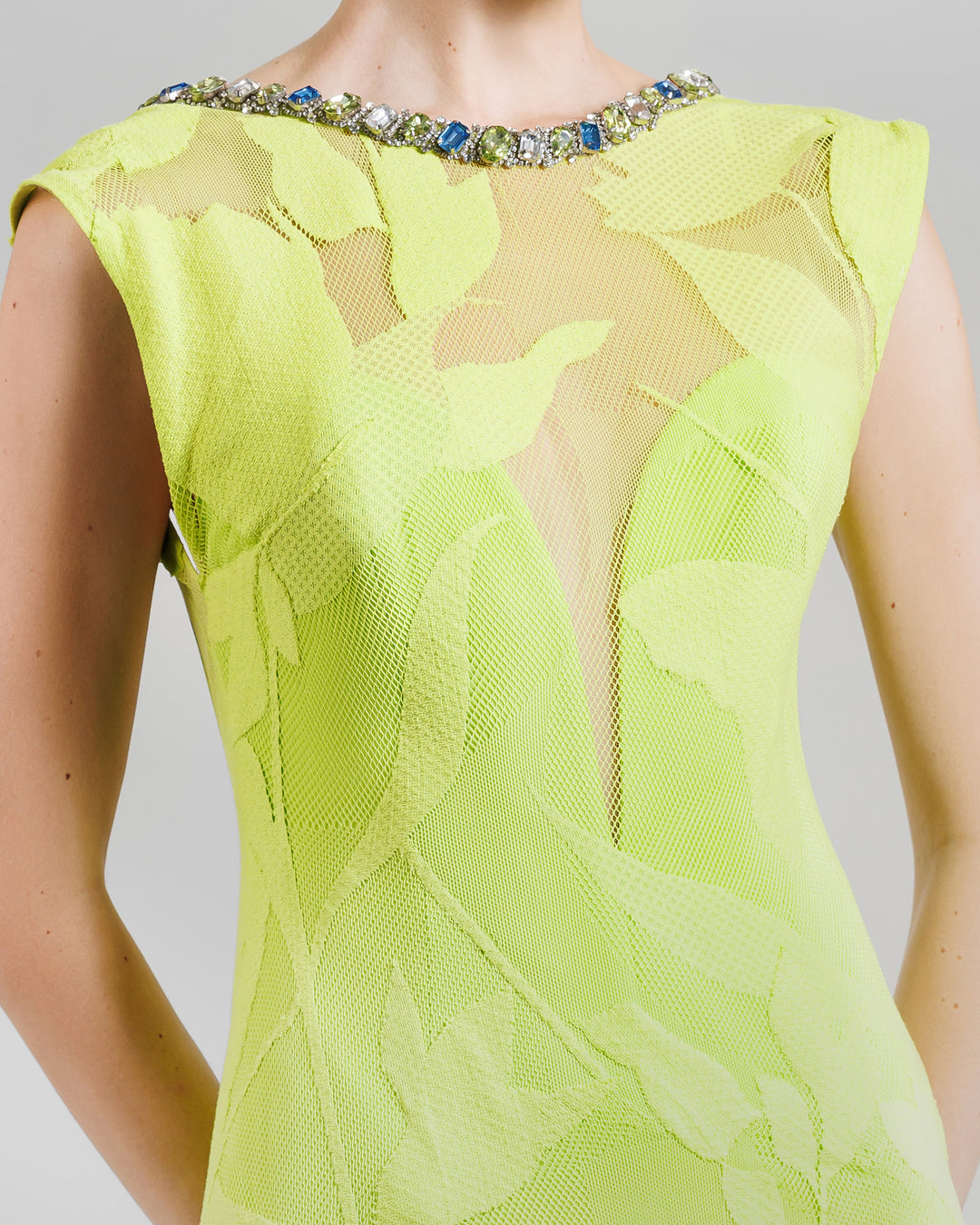 A close-up of a patterned lace fabric dress, with a deep V-neckline bodice under the sheer lace fabric. It features beads lining the round neckline.