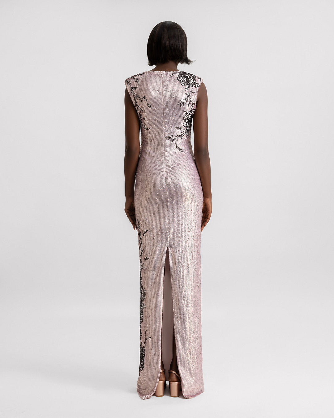 The back of a slim-cut embroidered sequins evening dress with structured shoulders, black floral embroideries, and  a slit at the back.