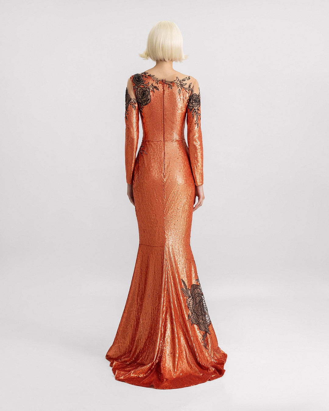 The back of a long-sleeve embroidered sequins dress in copper color with a small tail and black floral beadings.