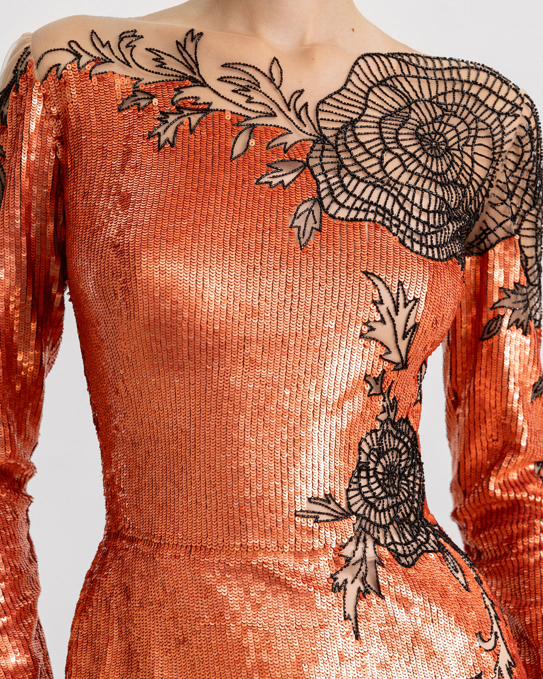 A close-up of a long-sleeve embroidered sequins dress in copper color with a small tail and black floral beadings.