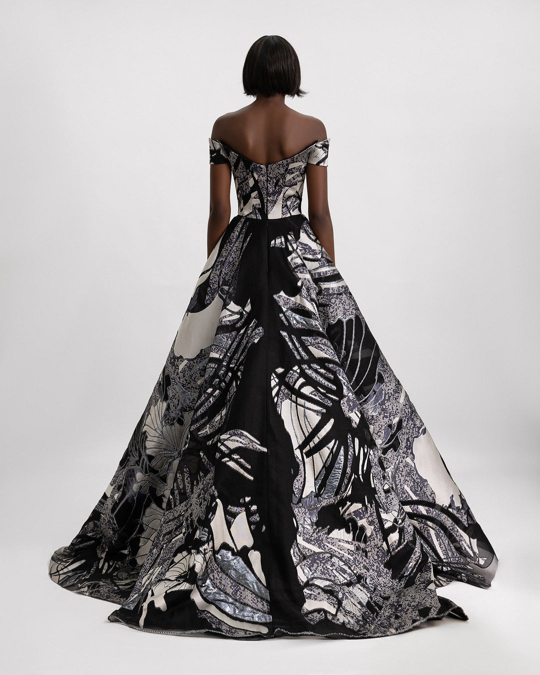 The back of an off-the-shoulders evening gown featuring a wide draped skirt in a printed jacquard devoré in black, grey hues, and champagne color.