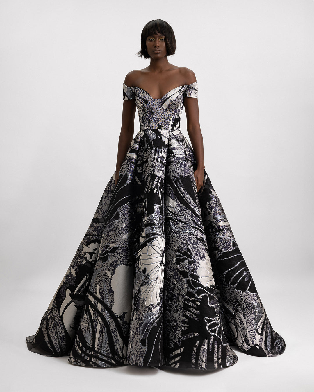 An off-the-shoulders evening gown featuring a wide draped skirt in a printed jacquard devoré in black, grey hues, and champagne color. 