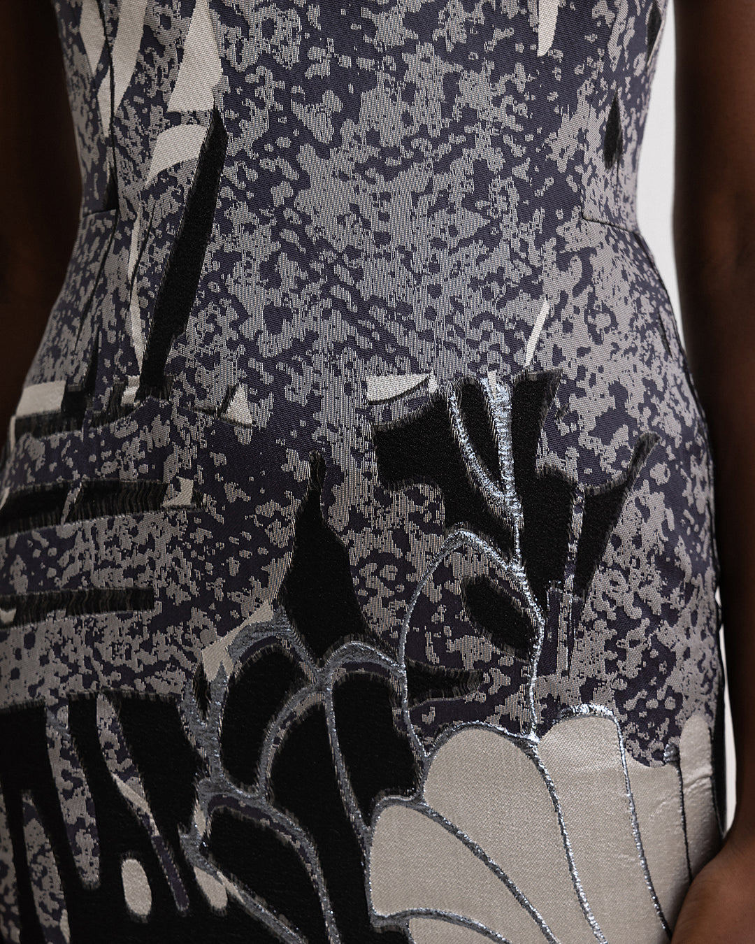 A close-up of a slim cut evening dress, in a printed jacquard devoré in black, grey hues, and champagne color.