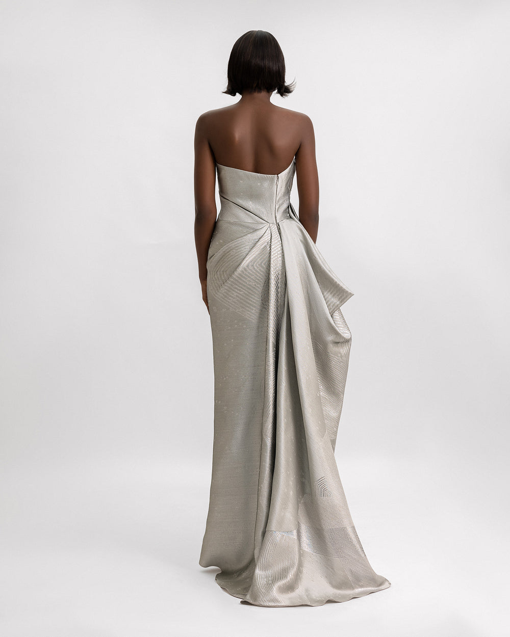 The back of a An asymmetrical strapless evening dress in greige jacquard with draped details on the side.