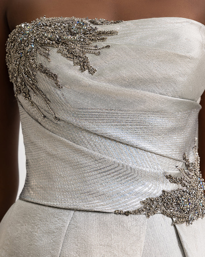 A close-up of a strapless draped evening gown in greige jacquard with beaded details on the corset.