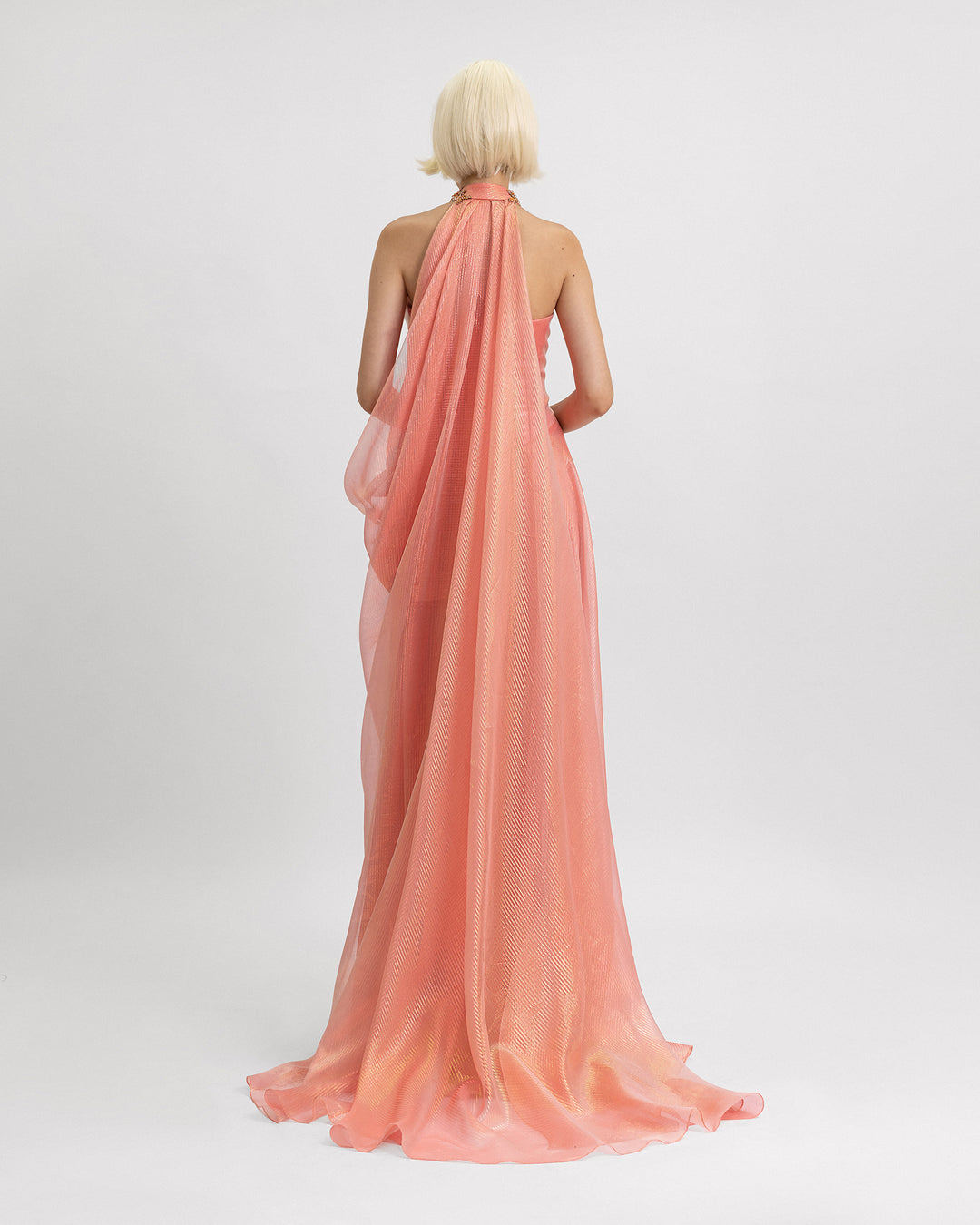 The back of a strapless draped evening dress in coral color featuring a beaded collar and a draped cape-like detail.