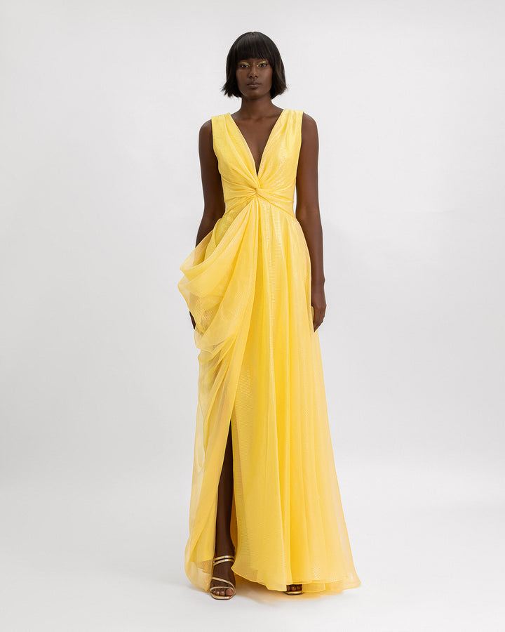 A v-neckline evening dress in yellow organza lamé with draping details on the side and an open slit.