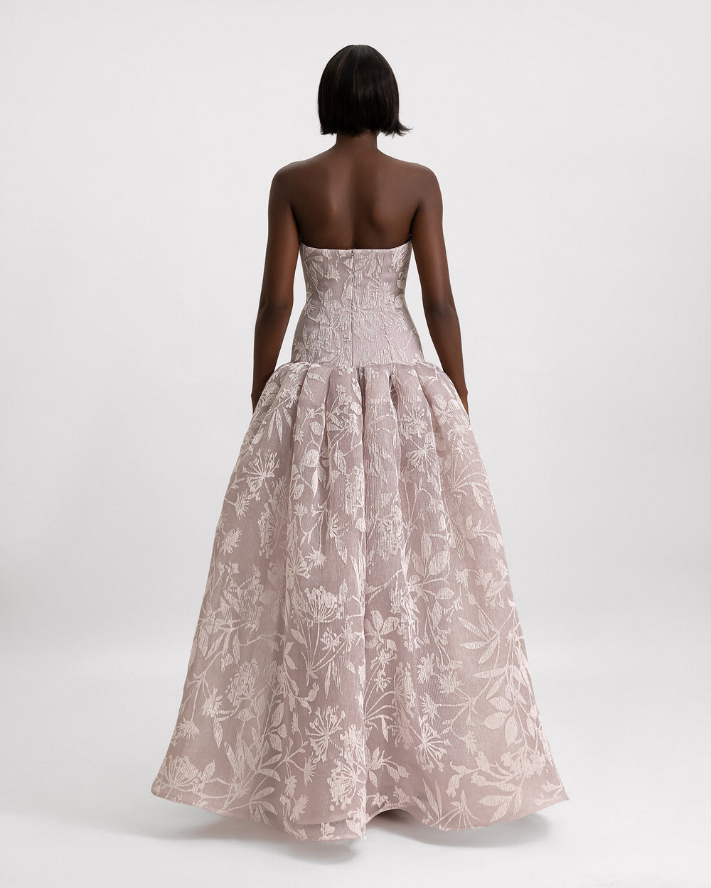 The back of a strapless evening dress in printed pleated organza jacquard with a dropped-down waistline and a draped skirt.