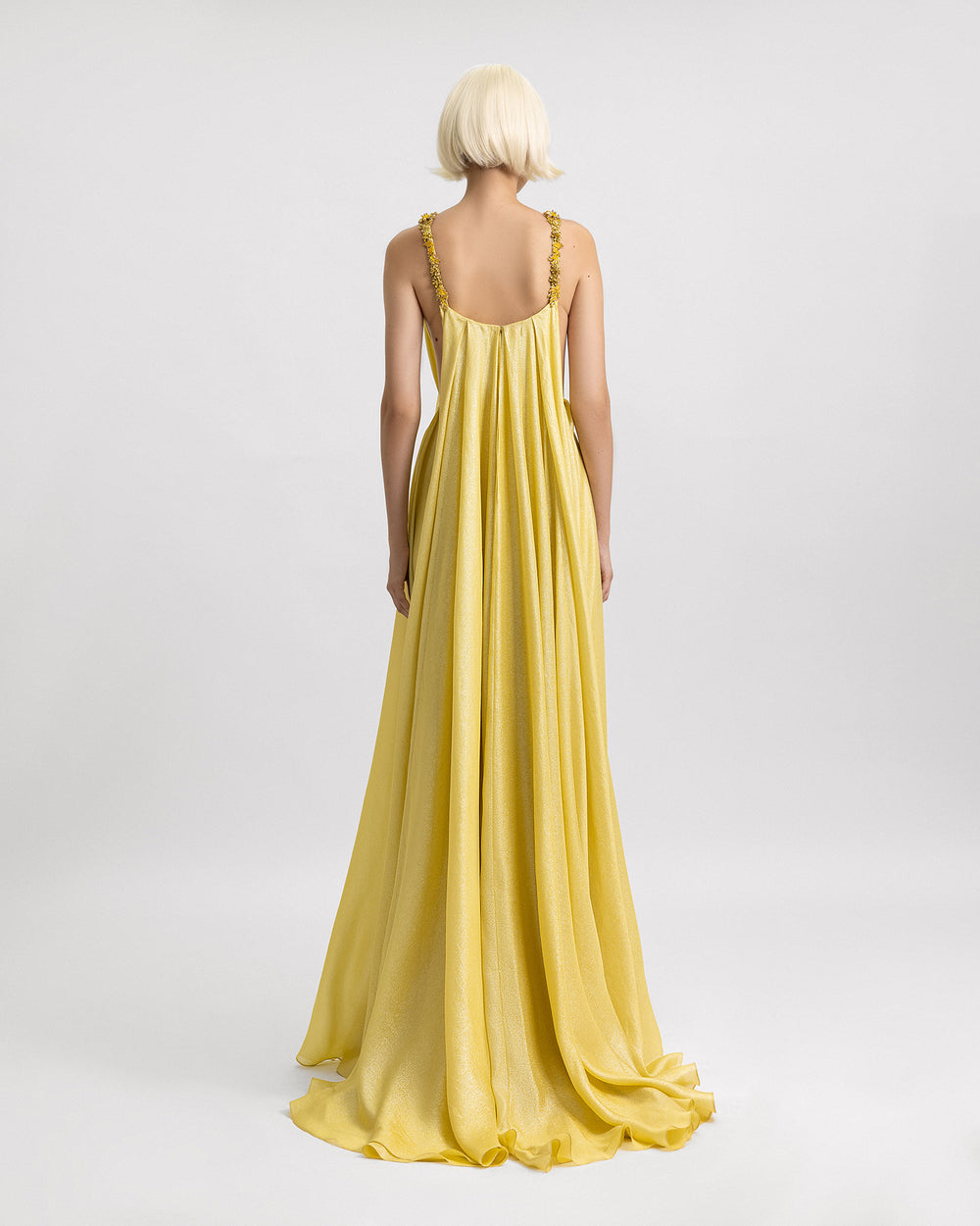 The back of a loose-cut yellow evening dress with beaded straps, and side openings on the corset.