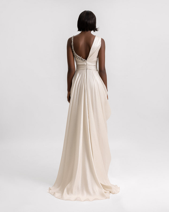 An asymmetrical open-back evening dress in greige color with one single side beading details and a draped skirt.