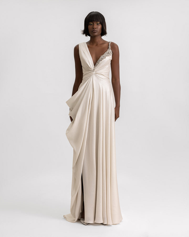 An asymmetrical neckline dress in greige color with neckline beading details, a draped skirt, and a slit on the side.