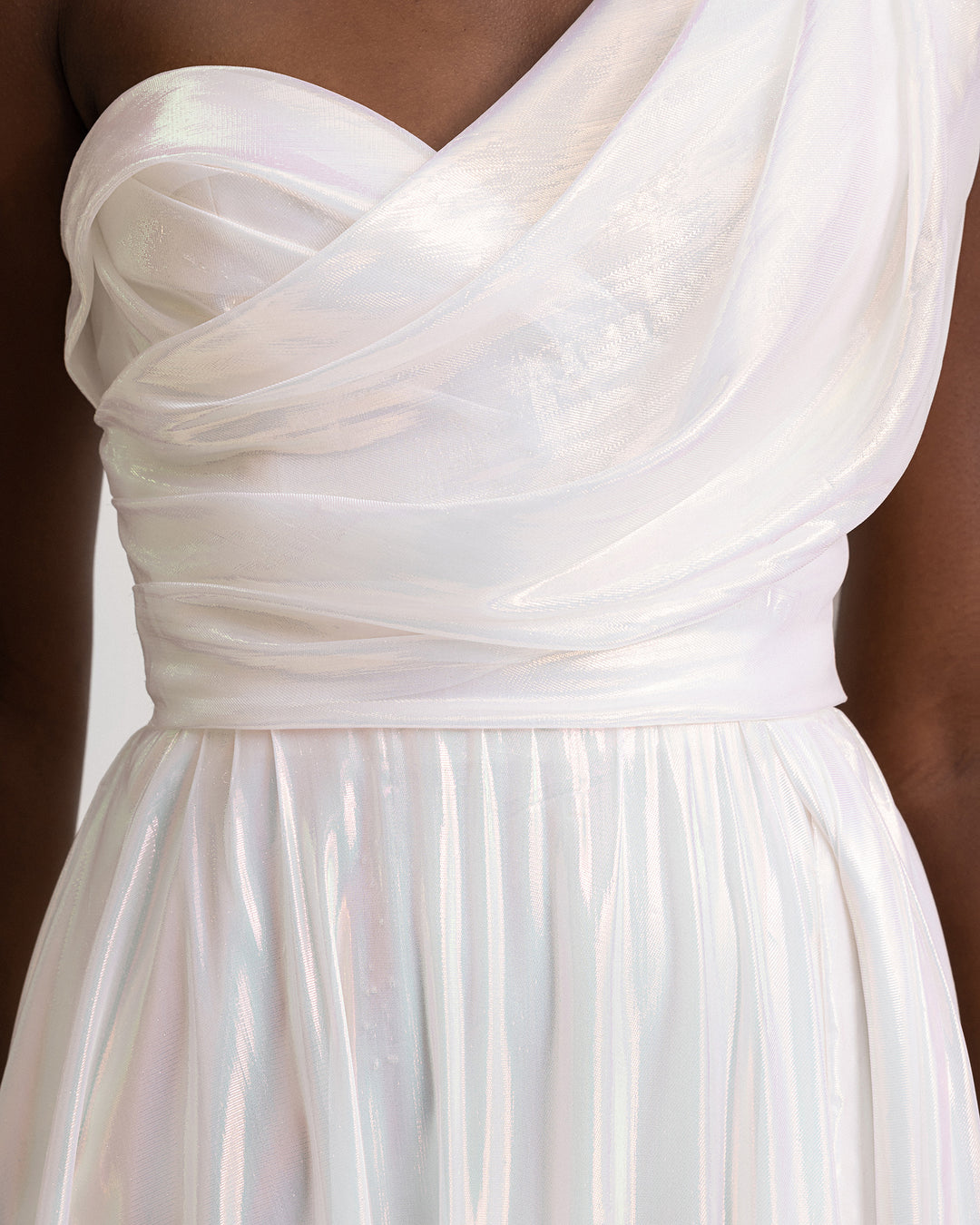 A close-up of a one-shoulder draped chiffon irisé dress in ivory with a slit on the side.