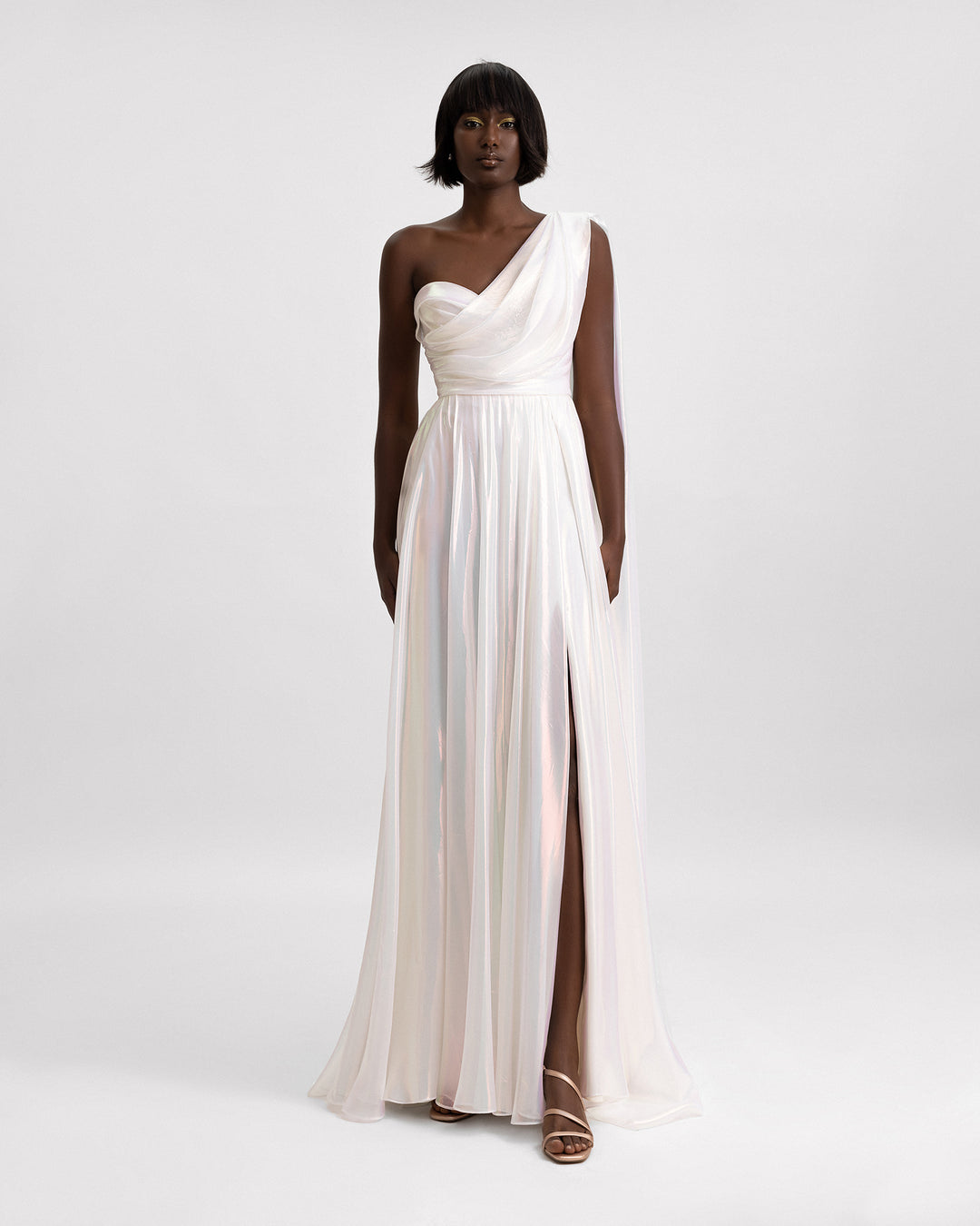 A one-shoulder draped chiffon irisé dress in ivory with a slit on the side.