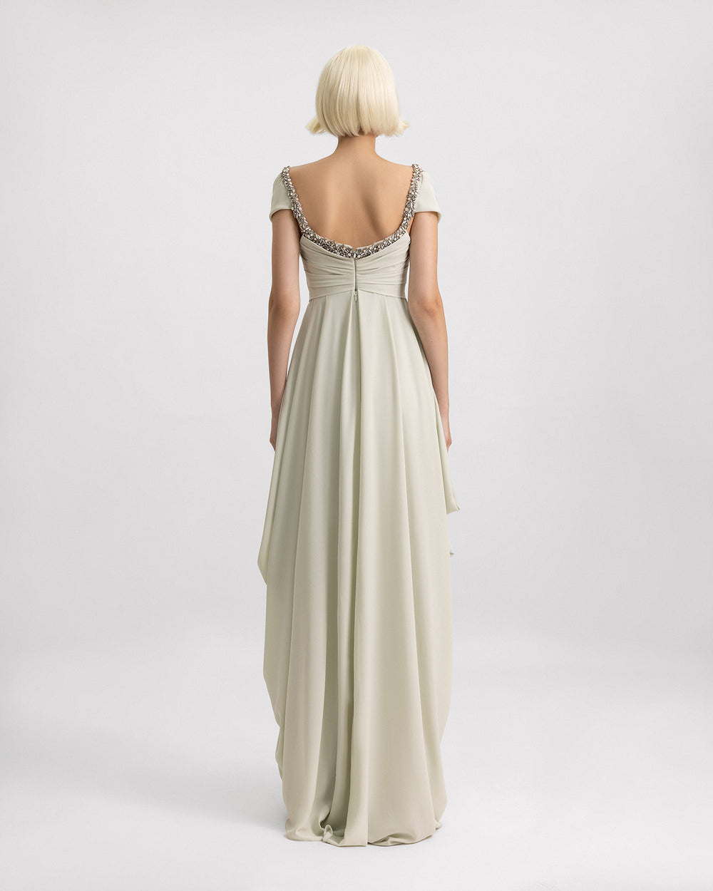 The back of a long evening dress in pale sage featuring off-the-shoulders draping, beaded neckline, and draped skirt on the sides.