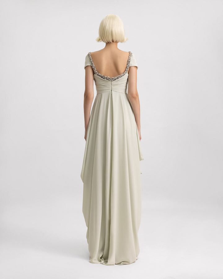 The back of a long evening dress in pale sage featuring off-the-shoulders draping, beaded neckline, and draped skirt on the sides.