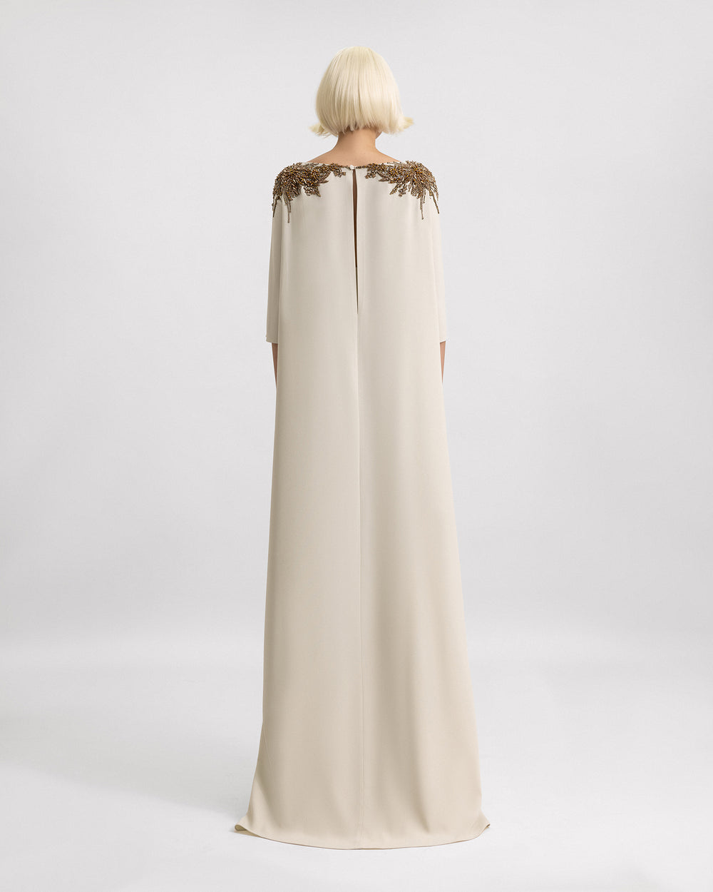 The back of a three-quarter sleeves evening dress in pale sage with beadings on the shoulders and a cape-like back.