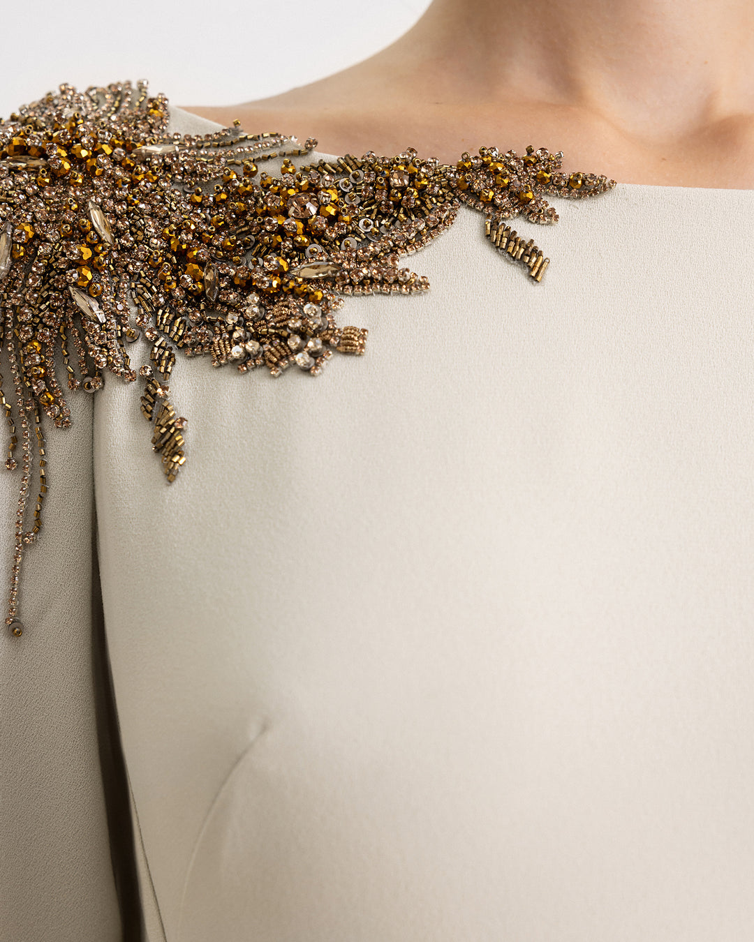 A close-up of an evening dress in pale sage with beadings on the shoulders.