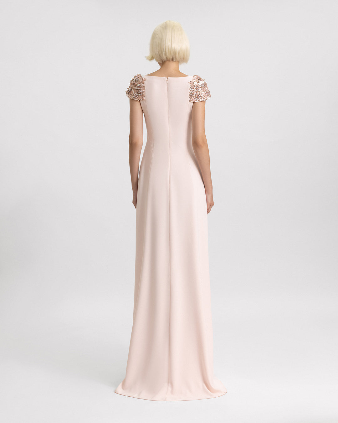 The back of a long evening dress in light pink with structured beaded shoulders.