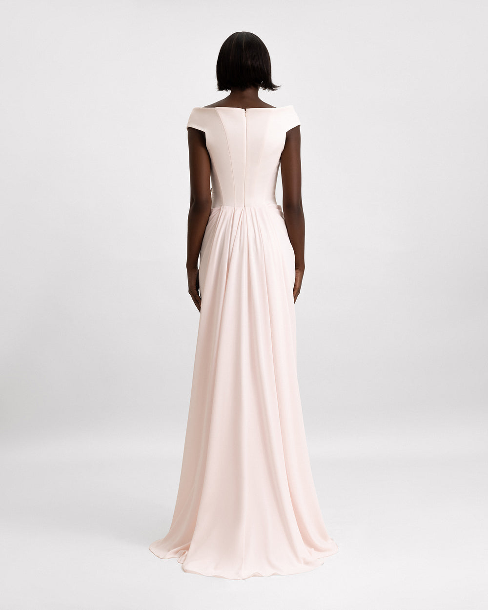 The back of an off-the-shoulders evening dress in light pink featuring a structured corset and a draped skirt.