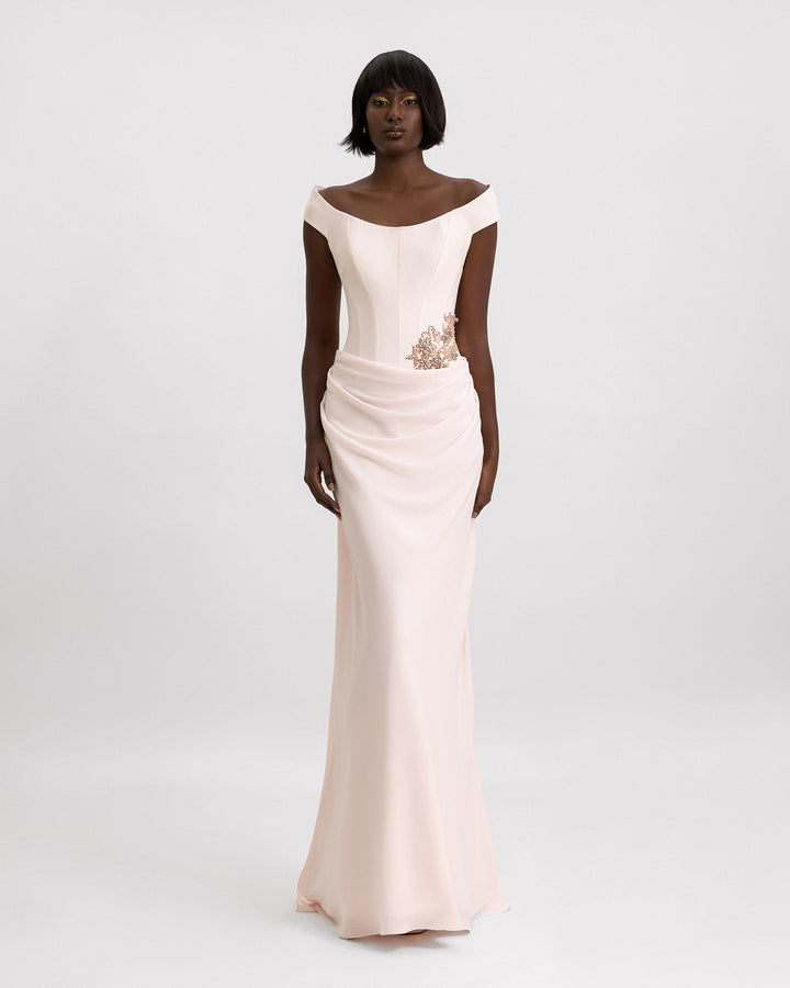 An off-the-shoulders evening dress in light pink featuring a structured corset, beading details on the waist, and a draped skirt.