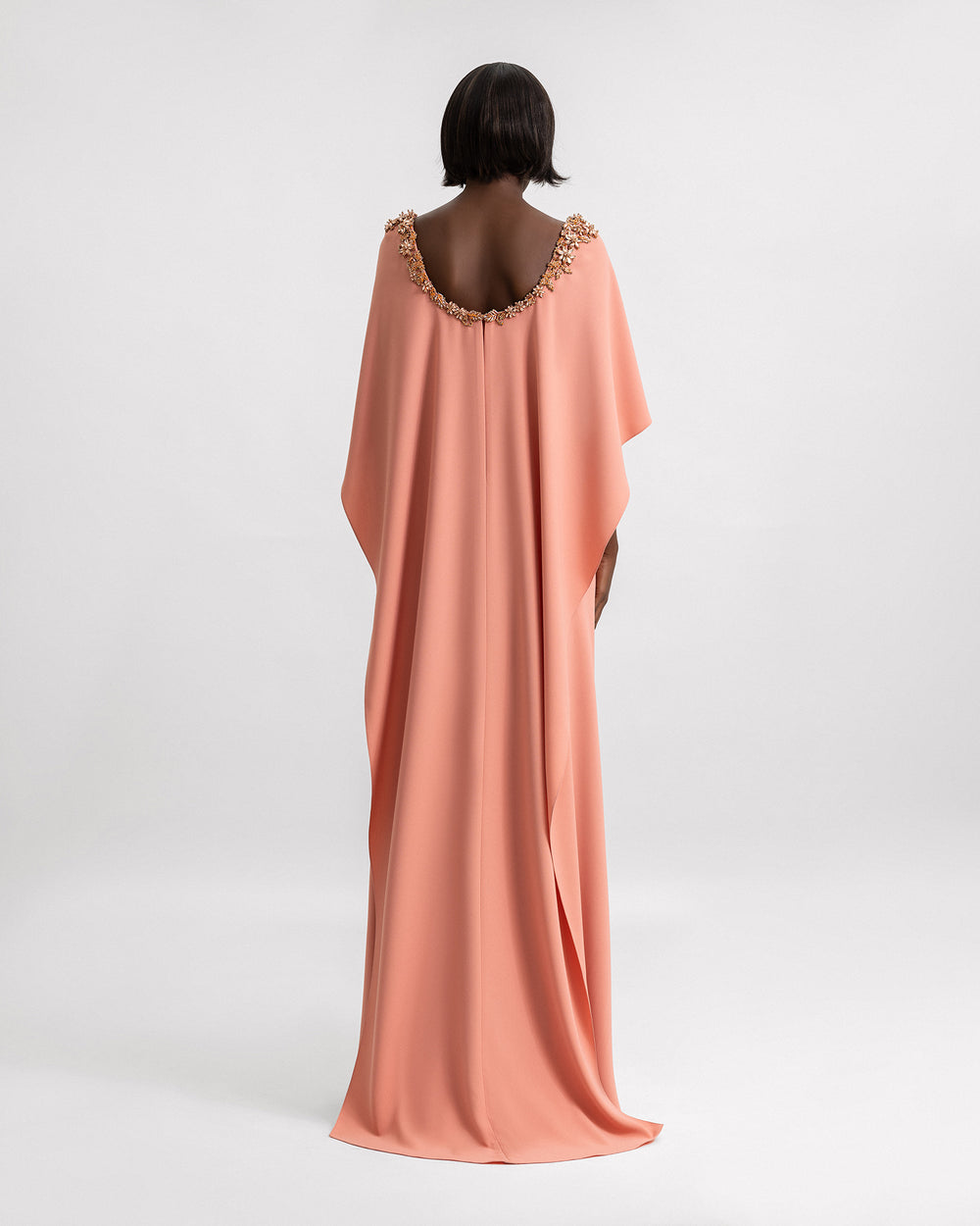 The back of a coral evening dress with beading details on the neckline and a cape.