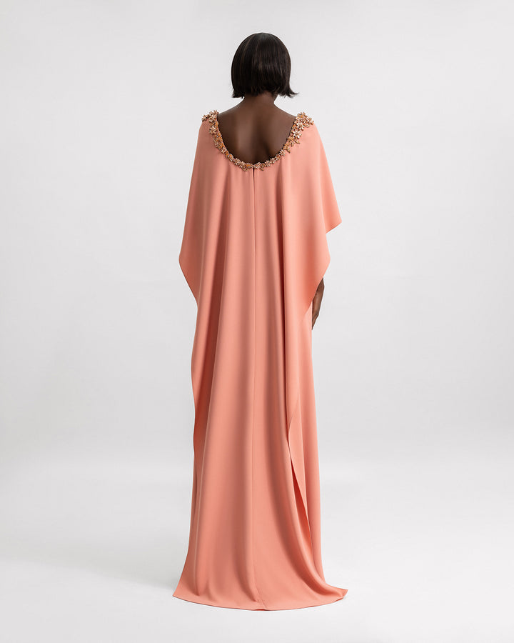 The back of a coral evening dress with beading details on the neckline and a cape.