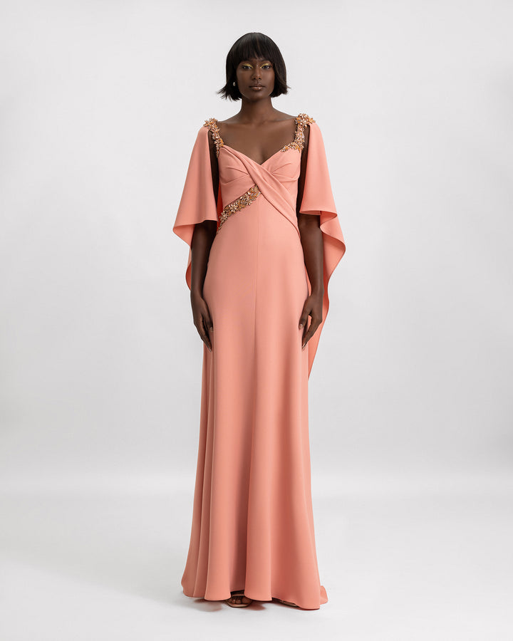 A slim-cut coral evening dress with beading details on the straps and cape-like sleeves.