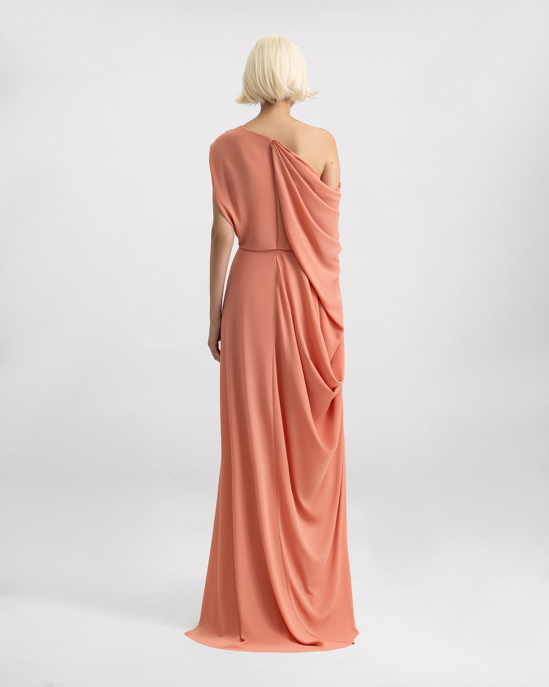 The back of a one-shoulder draped evening dress in coral color with a single side draping. 