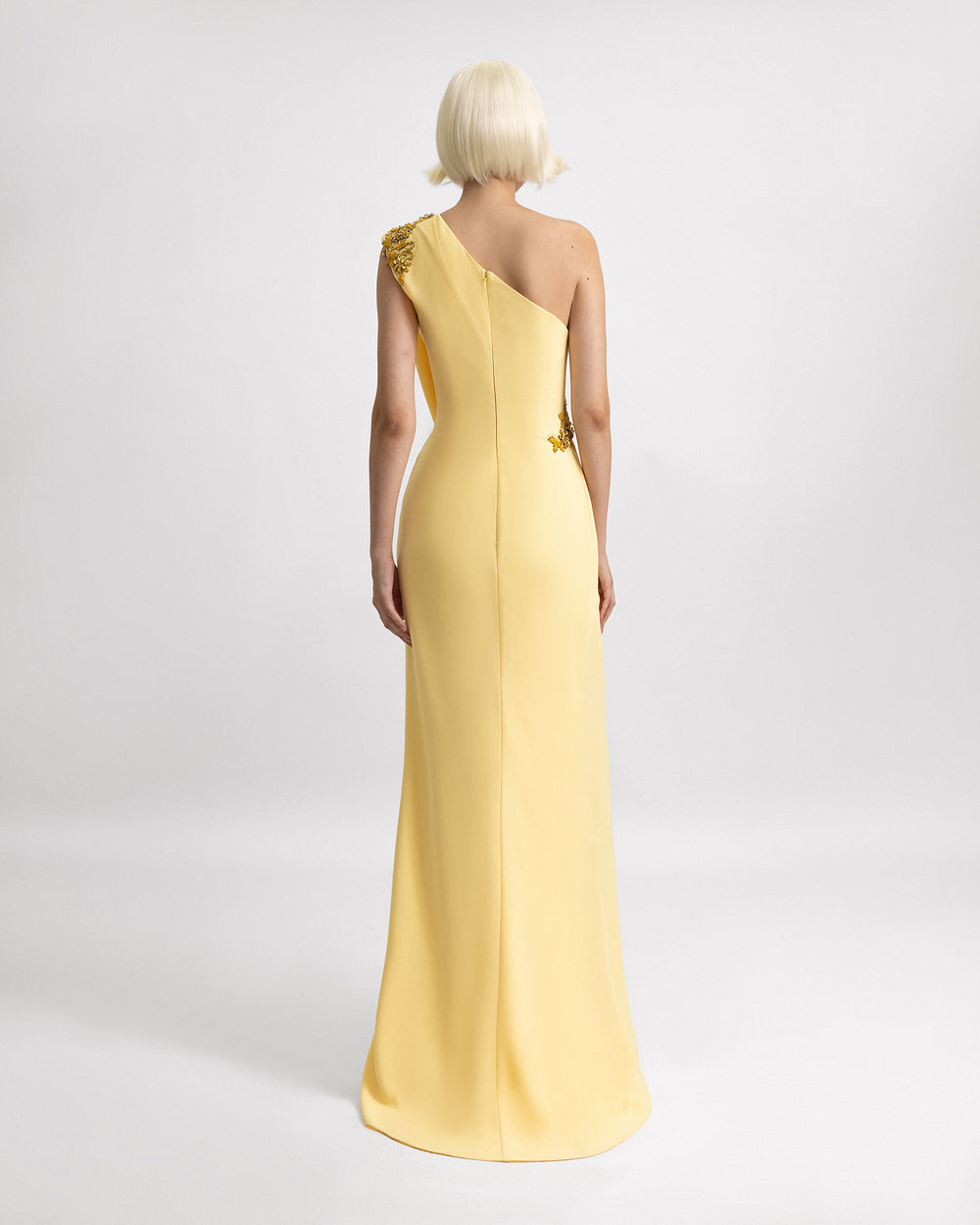 The back of a one-shoulder yellow evening dress with beading details on the shoulder and the waist.