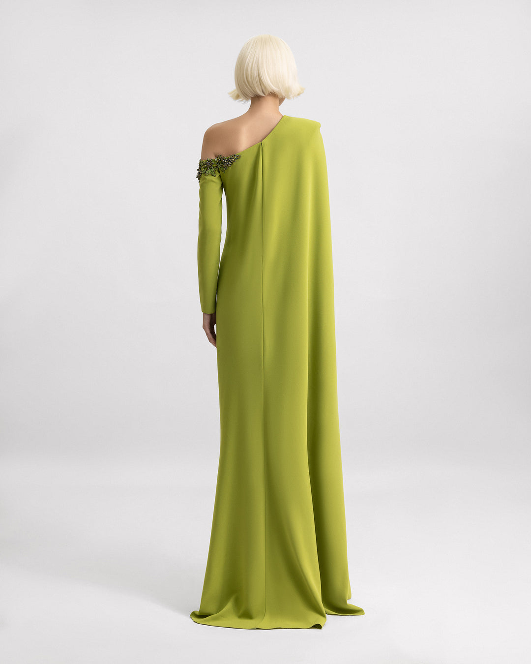 The back of a one-shoulder green evening dress with beadings on the neckline and a cape-like sleeve.
