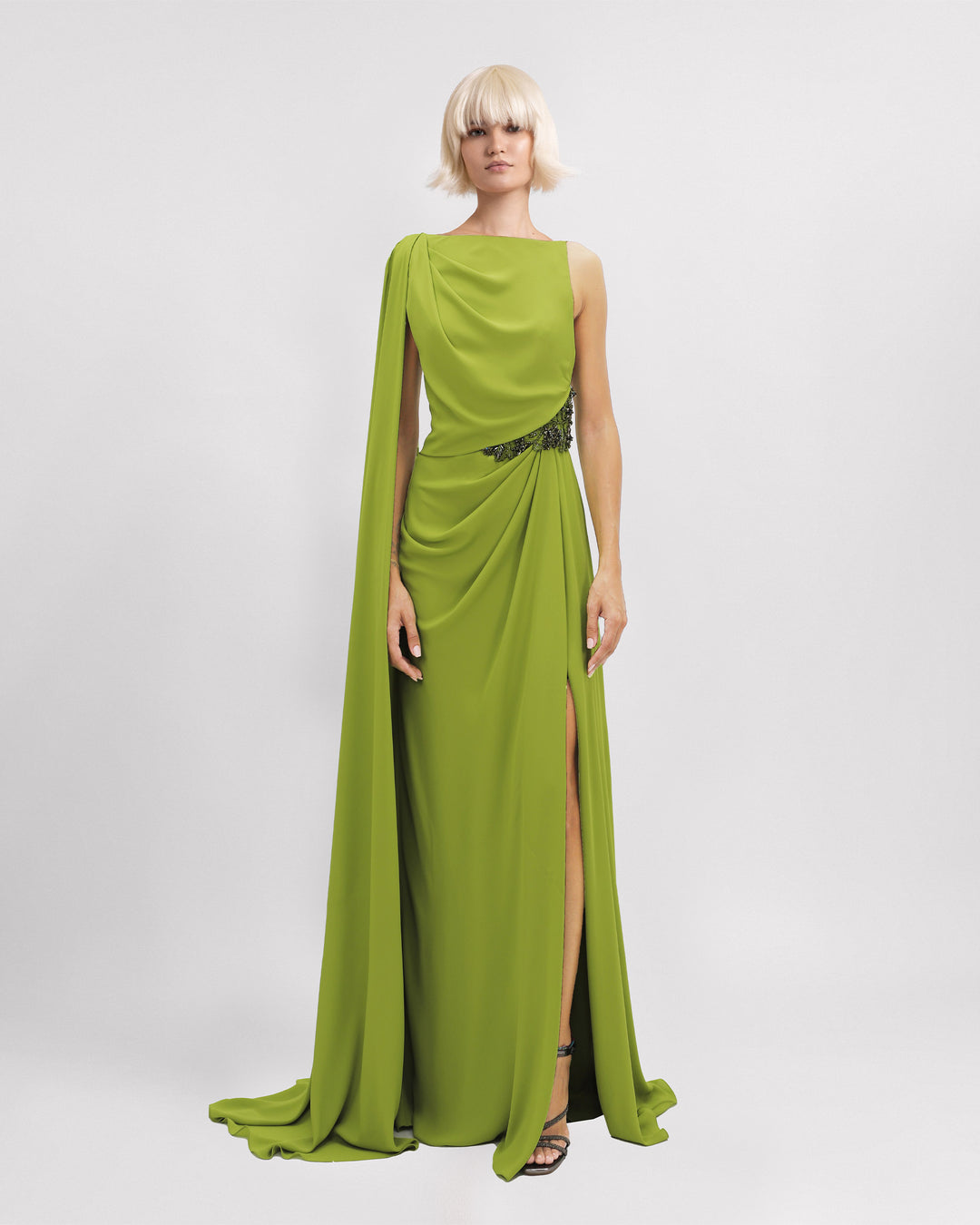 An asymmetrical neckline evening dress with beadings on the waistline, a cape-like sleeve, and a slit on the side.