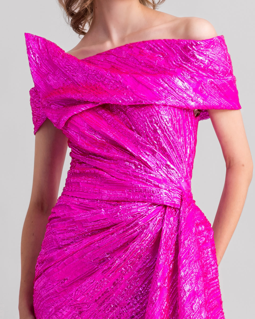 A close-up of an An asymmetrical neckline, off-the-shoulders fuchsia evening dress with a draped waist.