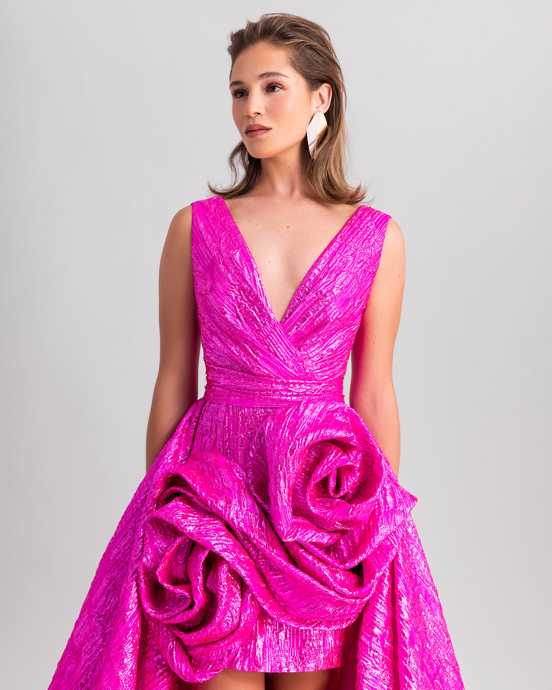 A close-up of a deep v-neckline fuchsia evening dress featuring big draped flowers and a wide draped tail.