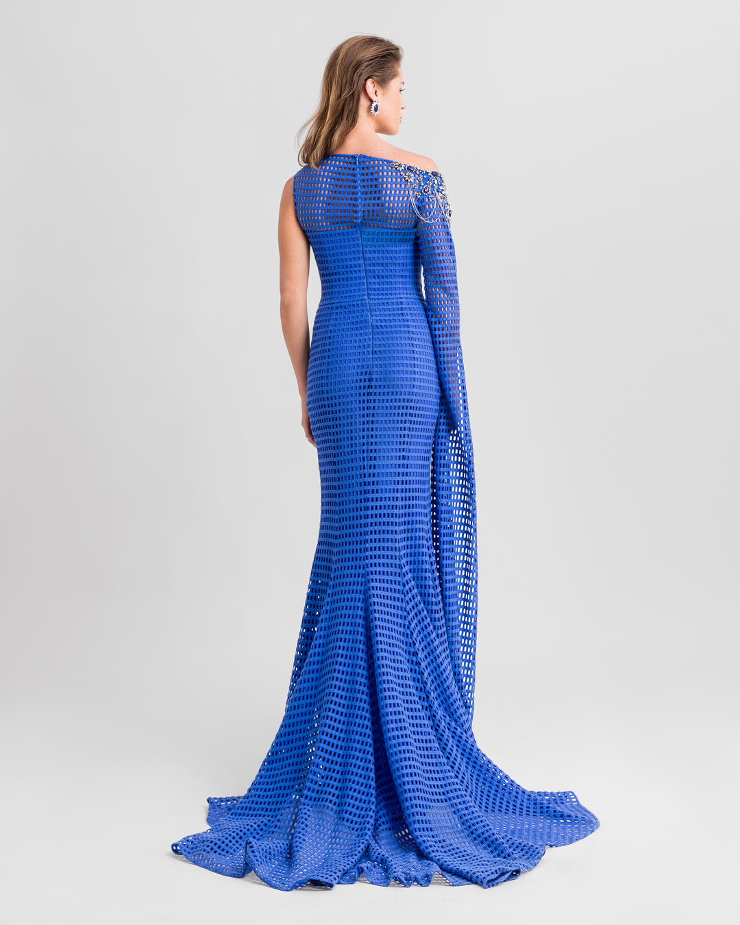 The back of an asymmetrical neckline crochet lace blue dress featuring a beaded shoulder, and a long flowy floor-length sleeve.