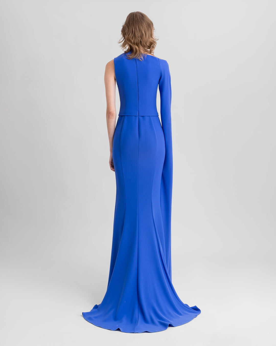 The back of an asymmetrical neckline blue evening dress with draping on the shoulder and waist, and a floor-length sleeve.