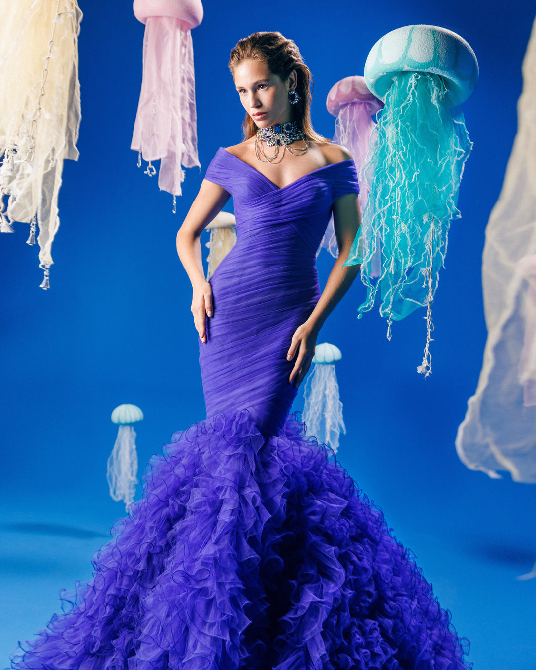 An off-the-shoulders draped mermaid-cut blue evening dress with rushed tulle at the bottom.