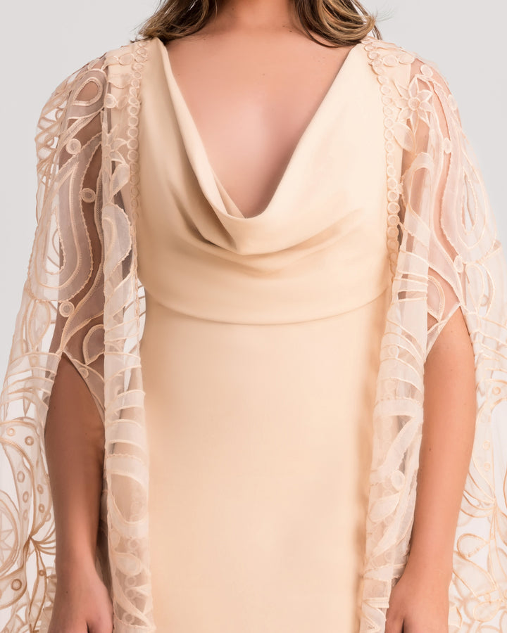 A close-up of a cowl neckline beige evening dress, paired with a wide patterned lace cape.